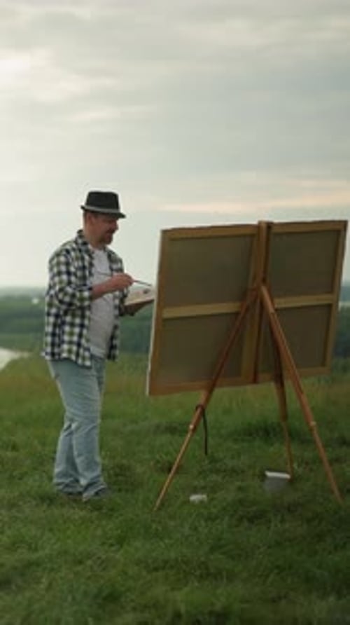 Artist Painting on a Large Canvas in a Tranquil Field By a Lake