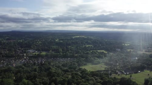 Aerial shot of the English countryside with a small village surrounded by forest and fields, smoke i