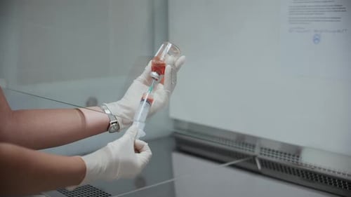 Doctor's Hand Holds a Syringe and a Orange Vaccine Bottle at the Hospital