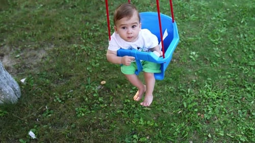 Sweet little Caucasian boy looking into camera swaying in a swing. High angle view.