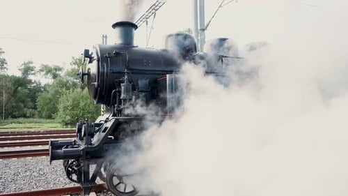 A departing steam historical train disappears into the distance and a thick cloud of white steam. Cz