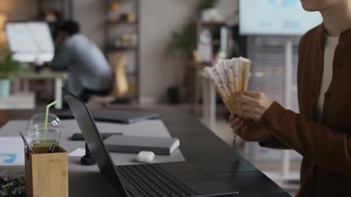 Asian Woman Cooling Herself with Hand Fan Working on Laptop at Office