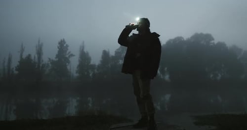 Man, night and forest with coffee, drink or torch on head for vision, tech