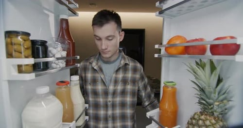 A Young Man Takes a Bottle of Juice From the Refrigerator View From Inside the Refrigerator