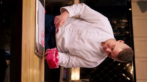 Vídeo vertical en el que un chef de una cocina profesional se pone de pie junto a la mesa y extiende una crema de dulces rosados