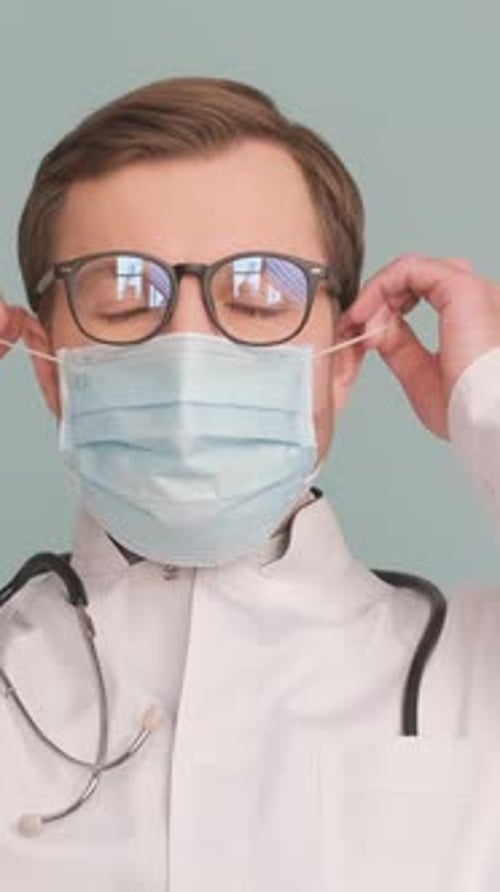 Portrait of a Doctor Taking Off a Protective Mask Isolated on a Gray Background