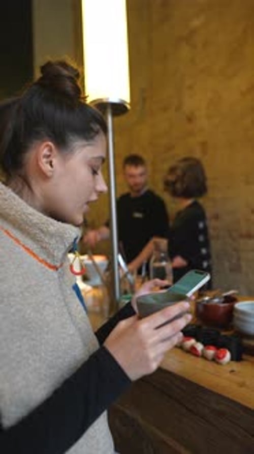 Young Girl Sitting at Coffee Shop with Mobile Phone Drinking Coffee and Looking at Mobile Screen