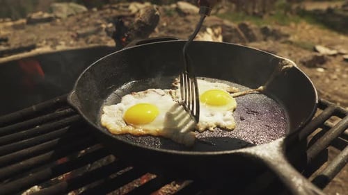 Close up cooker using spatula to adjust two fried eggs in the pan