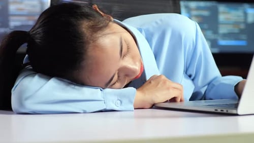 Gros plan d'une programmeuse asiatique endormie pendant qu'elle écrit du code sur un ordinateur portable à l'aide de plusieurs moniteurs