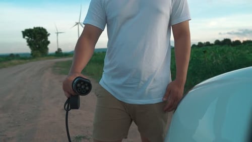 Progressive man with his EV car and wind turbine as concept of renewable energy.