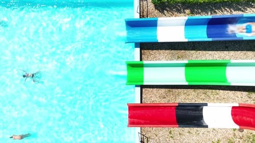 Super slow motion aerial view of man sliding down water slide at aquapark. Man splashdown into the p