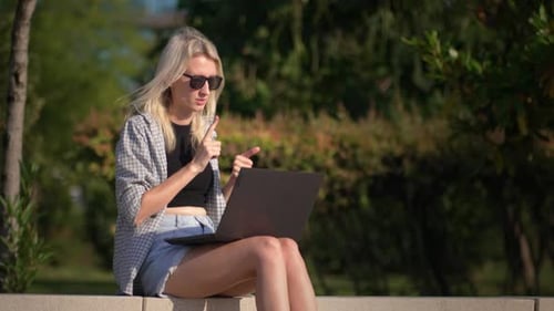Beautiful young freelance woman with laptop lying sitting on bench in park.