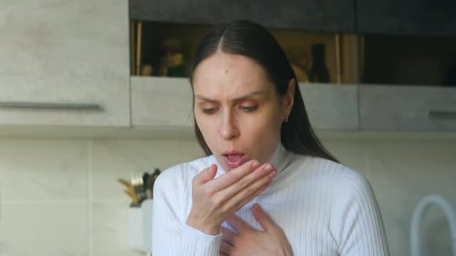 Woman in Kitchen Coughing While Holding Chest