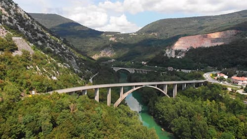 Drone shot of two giant bridges and a river flowing below, trees and town visible nearby, cars drivi