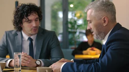 Businessman Discussing Documents with Senior Executive in Cafe