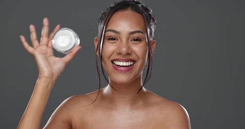 Happy woman, face and cream for skincare, beauty or cosmetics against a grey studio background