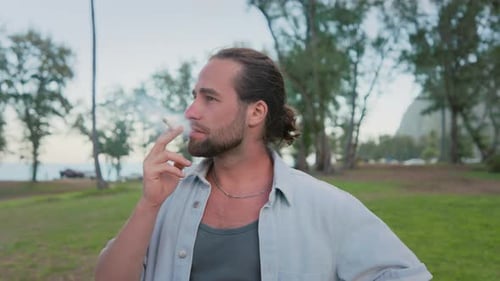Un homme fait une pause réfléchie dans un parc en train de fumer et de profiter d'une nature sereine