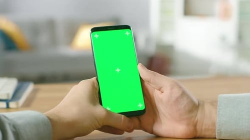 Close-up of a Man Holding Green Mock-up Screen Smartphone in His Hands. Using Modern High End Devic