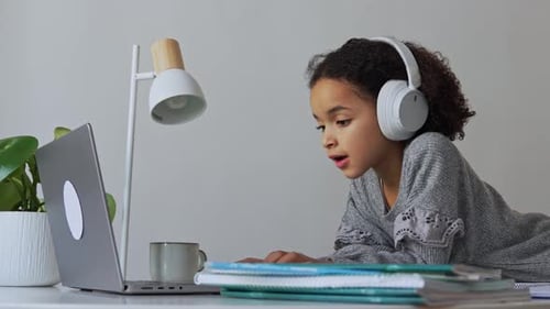 Primary School African American Student Child with Headphones Hand Writing in Book Using Laptop