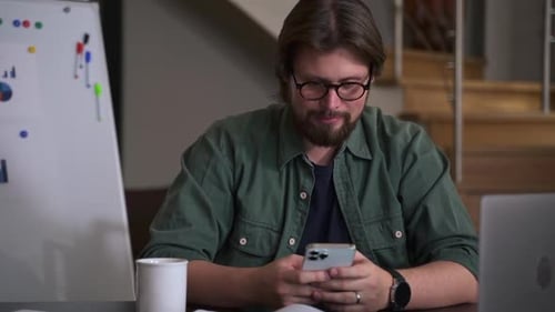 Young Businessman or Coach Using Smartphone and Thinking Sitting at Table in Modern Office Spbas