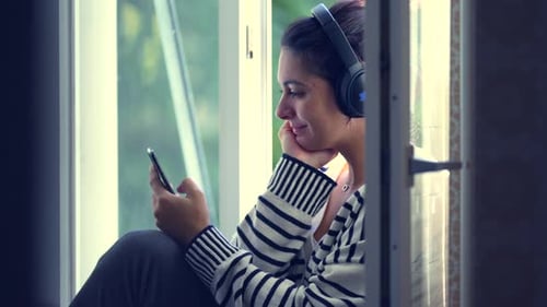 Woman Listening to Music with Headphones by Window