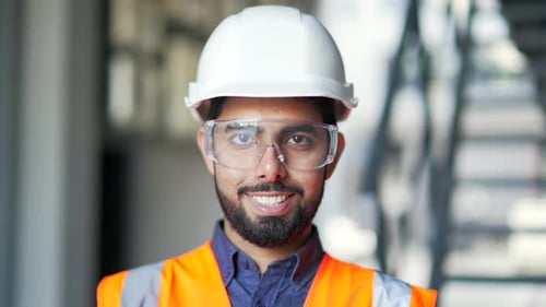Close up portrait of young smiling professional engineer wearing safety helmet, protective glasses