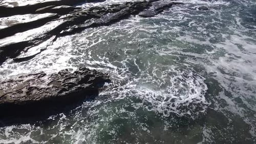 A drone shot starts close to the water, capturing waves crashing on rocks, then tilts up to reveal t