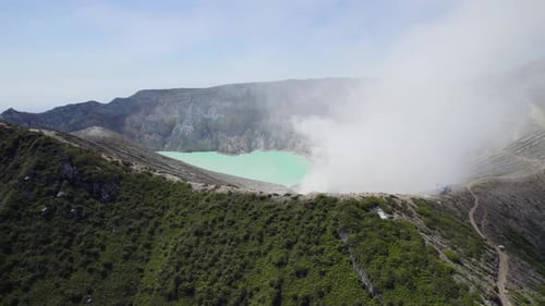 Aerial Closeup of the rim of a steaming volcano Ijen with a Turquoise Lake, and foggy cloudy Mountai