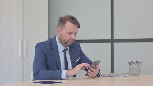Man in Suit Using Smartphone at Office Desk