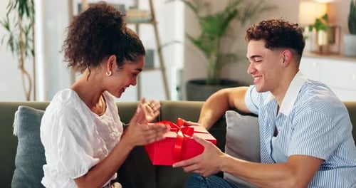Couple, amour et cadeau sur le canapé pour la Saint-Valentin, une fête ou un geste romantique à la maison