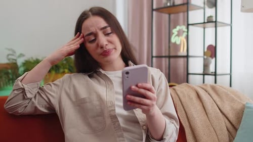 Annoyed Woman Using Phone on Couch Indoors