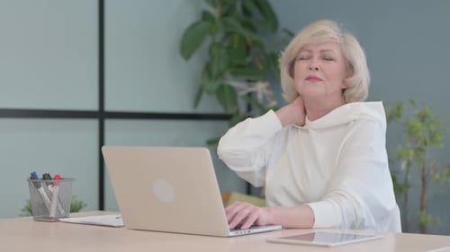 Senior Woman Types on Laptop Massaging Neck