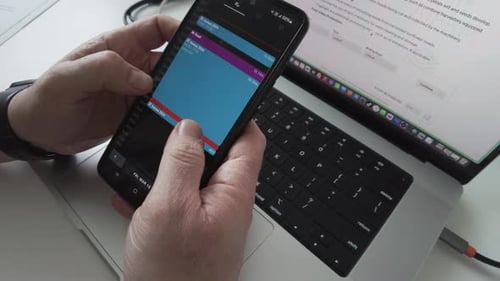 Hands Using Calendar App on Smartphone Above Laptop