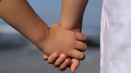 Nahaufnahme von Kindern, die sich eng an den Händen halten, Kinder halten sich an der Küste die Hände und beobachten die warmen Wellen