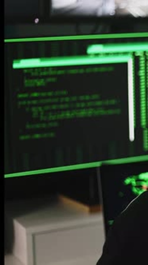 Hooded Figure Working at Computer Monitors in Dark Room