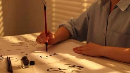 Kalligrafie. Frau mit Pinsel schreibt Satz Ich liebe dich auf ein Blatt Papier am hellen Holztisch