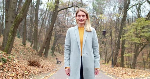 Young Beautiful Blonde Caucasian Woman Standing in Park in Cold Autumn Day Wearing Stylish Coat