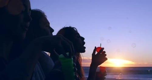 Friends, blowing bubbles and sunset on beach for happiness, bonding and celebration in summer