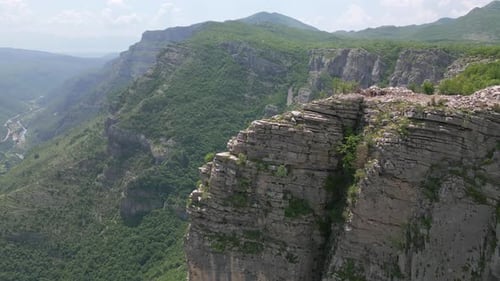 An epic rock against the backdrop of green mountains stretching into the distance.