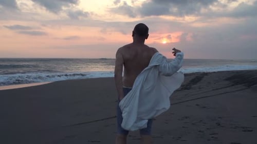 Man Puts on Shirt at Sunset Beach