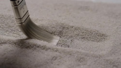 Paint Brush Sweeping Sand to Reveal Silver Object
