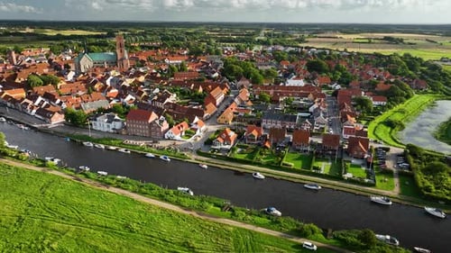 Camera pans along the riverside of Ribe with docked boats, tilting up to reveal the historic town Ri
