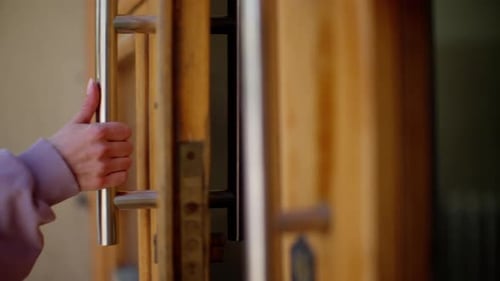 Closeup of Hand Gripping a Stainless Steel Handle on a Wooden Door