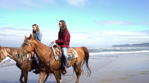 Two women enjoying a horseback ride on a beautiful beach at sunset