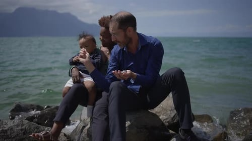 Family Sits Together on Rocky Beach by Ocean