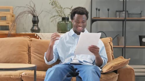 Man Reading Document Celebrates on Couch
