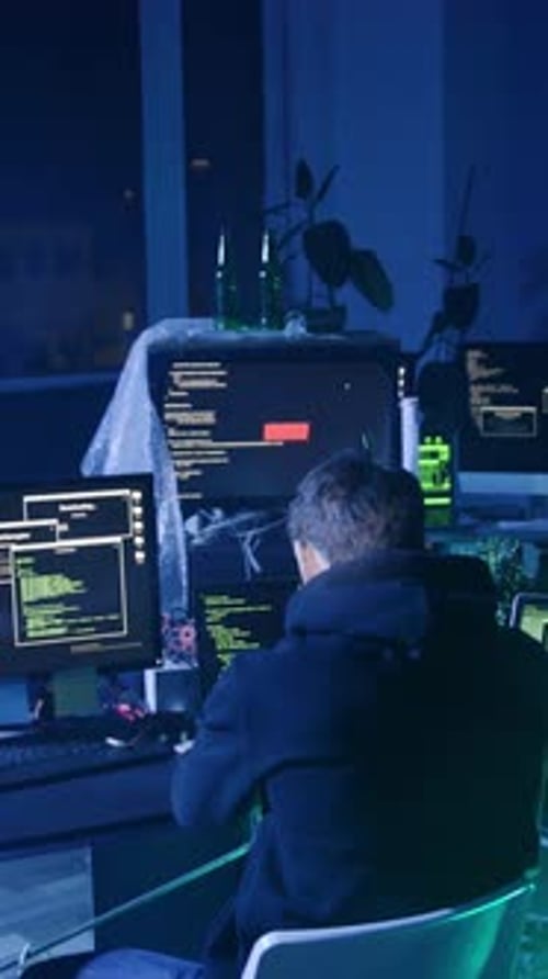 A Man in Sunglasses Works Intently at Dual Monitors in a Dark Room