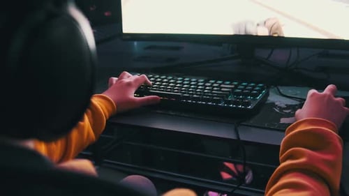 Boy in a Computer Club Sits By Monitor Playing Shooter Game on Gaming Chair