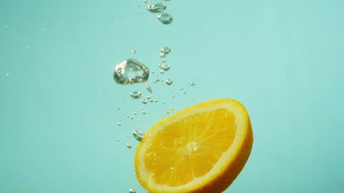 Ein Stück Grapefruit fällt ins Wasser und erzeugt Luftblasen