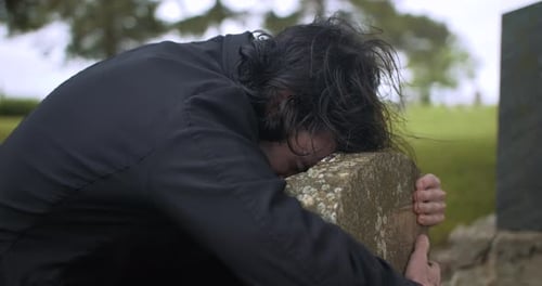 Sad, crying man grieving over grave in cemetery.